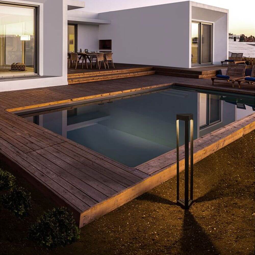 Pax Pollerleuchte Dreieck LED Schwarz neben modernem Pool auf Holzterrasse bei Abendstimmung.