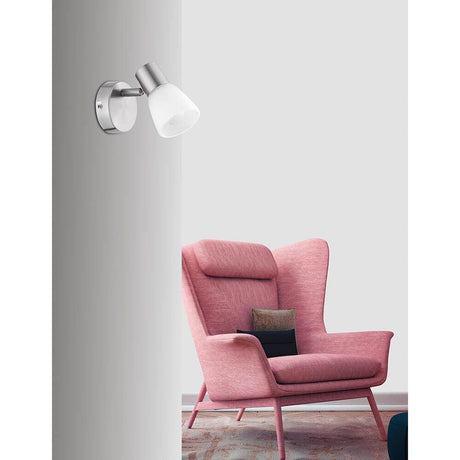 Publico Nickel Satin Wall Spot on a wall next to a modern pink armchair.