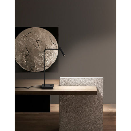 Sicily LED Tischlampe aus schwarzem Metall auf einem modernen Holztisch mit Kunstwerk im Hintergrund.