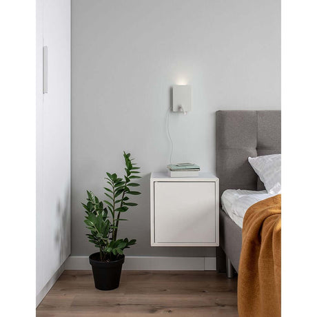 Zen LED vegglampe med lesearm og USB ved en vegg ved siden av sengen og et nattbord med plante.