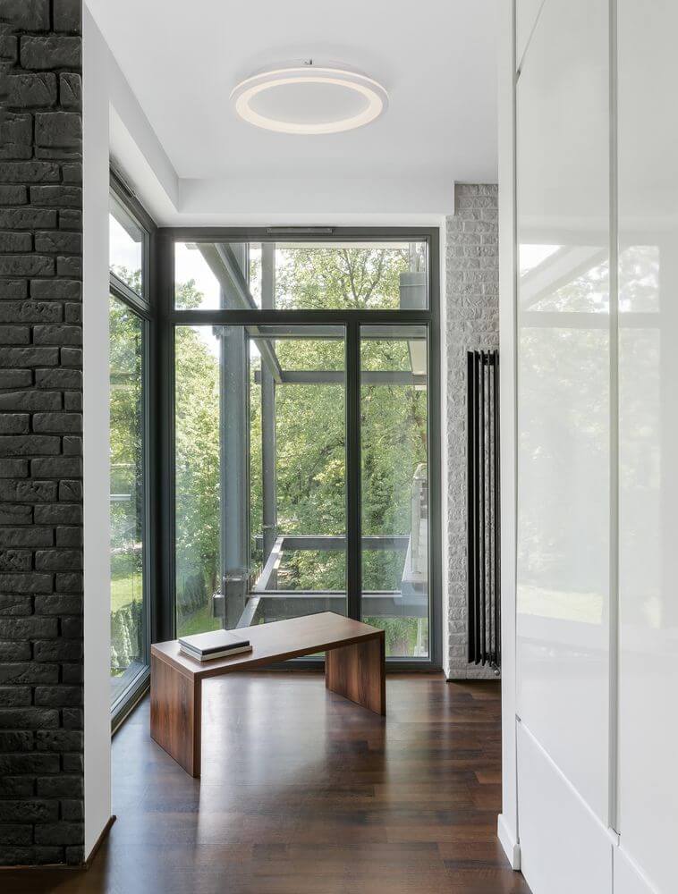 Oggy LED Deckenleuchte Ø 37cm 3000K im modernen Wohnraum mit großen Fenstern und dunklem Holzfußboden.