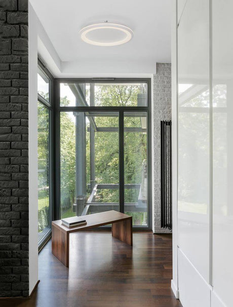 Oggy LED Deckenleuchte Ø 37cm 3000K im modernen Wohnraum mit großen Fenstern und dunklem Holzfußboden.