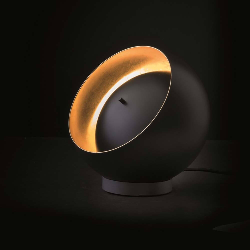 Oluce LED Tischleuchte Eva Schwarz, Goldfarben auf einem Tisch mit elegantem Design und einzigartiger Lichtwirkung.