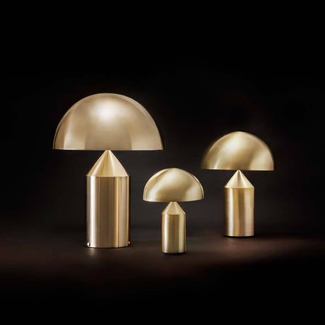 Lampe de table Oluce Atollo 35 couleur or en trois tailles sur fond noir.