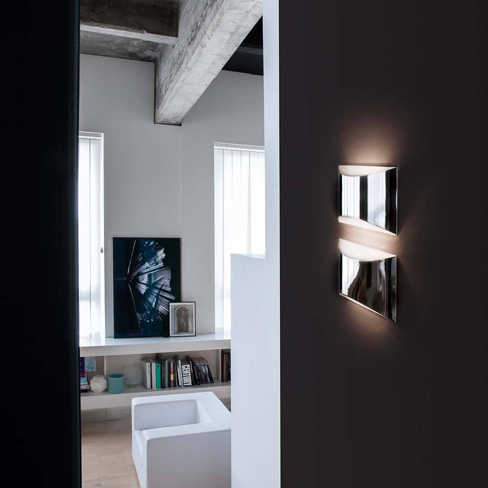 Oluce LED Wandlampe Kelly Chrom an einer Wand in einem modernen Wohnraum.