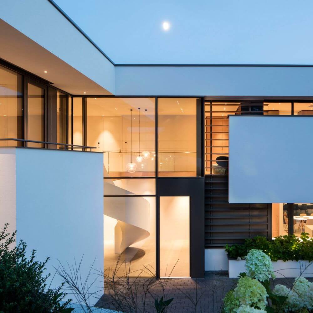 Moderne Architektur eines Hauses mit großen Fenstern und einer eleganten Fassade bei Abendstimmung.