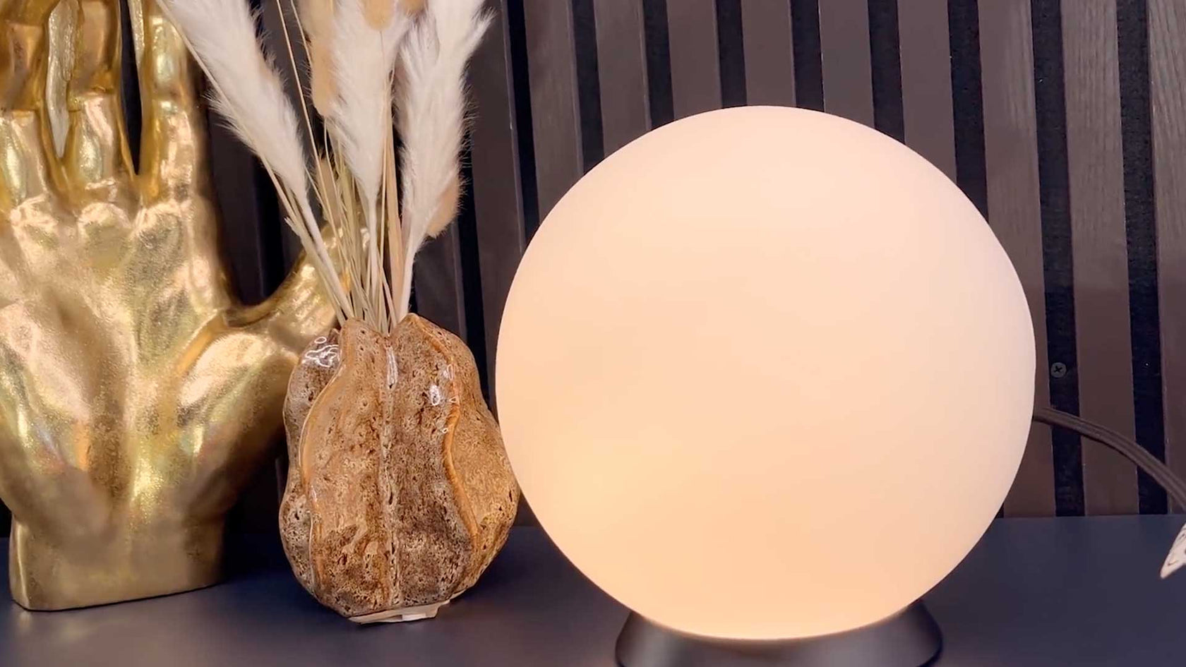 Dekorative Lampe mit sanftem Licht, daneben eine goldene Vase mit getrockneten Pflanzen.