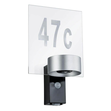 Hausnummernschild Outdoor House Transparent mit silbernem Nummernsatz und Wandleuchte im Eingangsbereich.