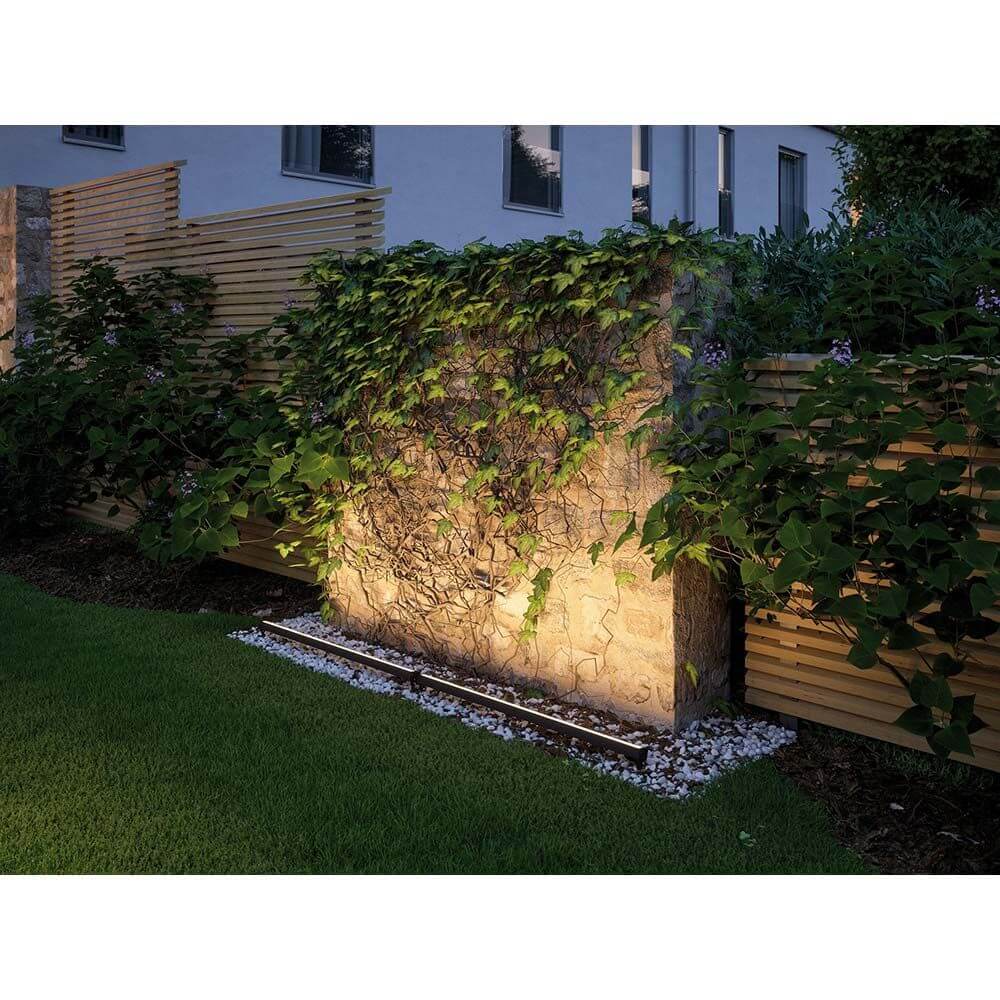 LED Plug & Shine Bodenaufbauleuchte 115° IP67 3000K Anthrazit beleuchtet eine Gartenmauer mit Pflanzen.