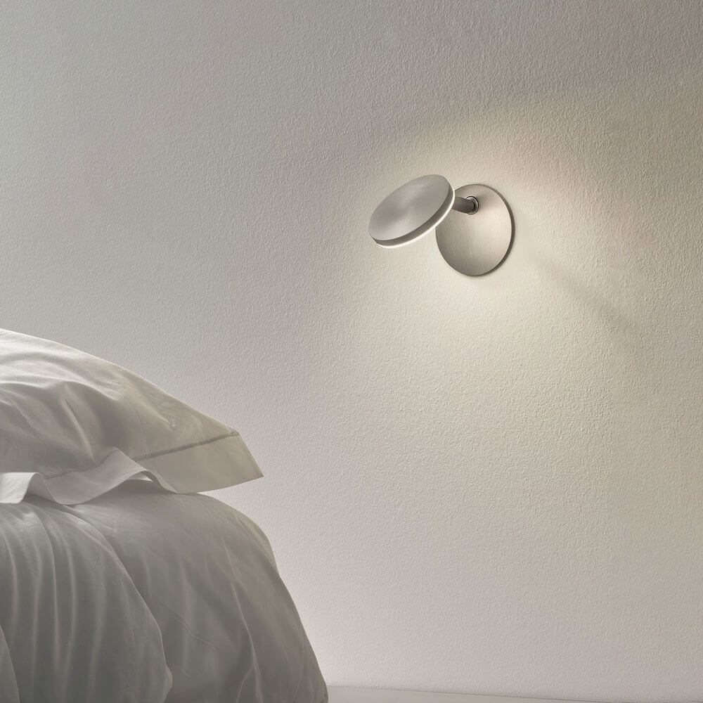 Panzeri Bella built-in LED wall lamp touch switch on a wall next to a bed with fresh white bedding.