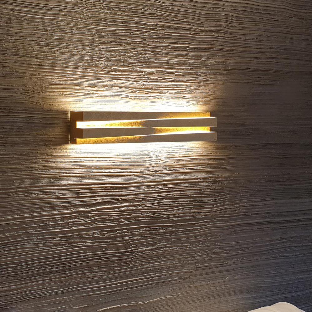 Panzeri Cross LED Wandlampe indirekt und direkt an einer strukturierten Wand mit warmem Licht.