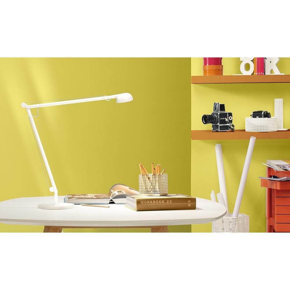 Panzeri Opuntia LED-Schreibtischlampe CCT-Dimmbar auf einem weißen Tisch vor gelber Wand mit Büromaterial.