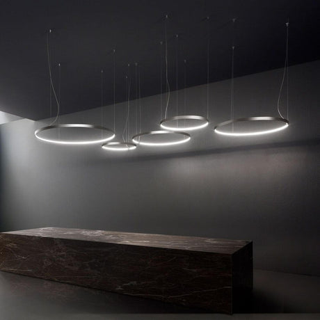 Panzeri Zero Round LED-Ring Pendelleuchte, elegante Hängeleuchte mit fünf runden Lichtringen über einem dunklen Tisch.