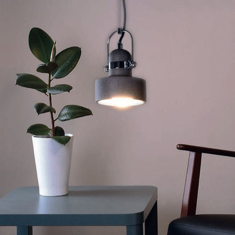 Pendentif en béton Pavo Ø 14 cm, style industriel, au-dessus d’une table avec une plante, moderne et élégant.