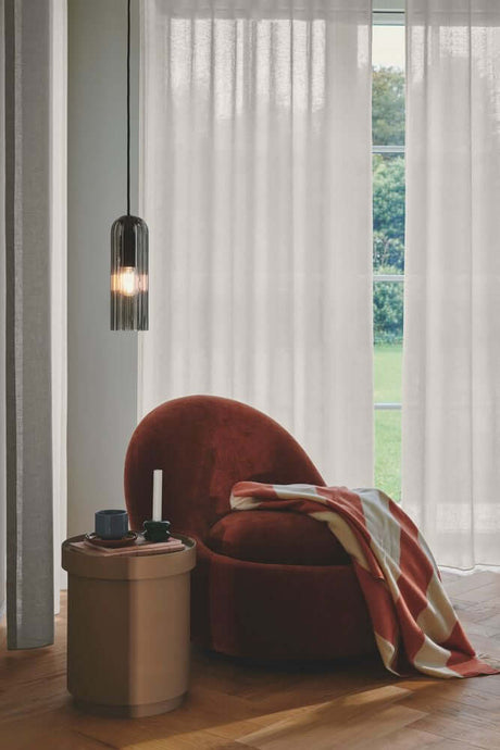 Pendelleuchte Miella über einem stilvollen rot gepolsterten Sessel in einem eleganten Raum mit großen Fenstern.