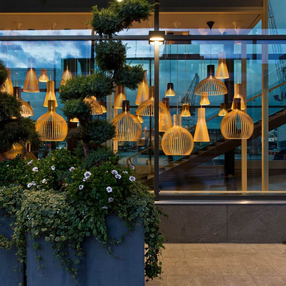 Pendelleuchten aus Holz im Schaufenster, dekoriert mit Pflanzen und einer modernen Architektur. Schöne Beleuchtungstechnik.