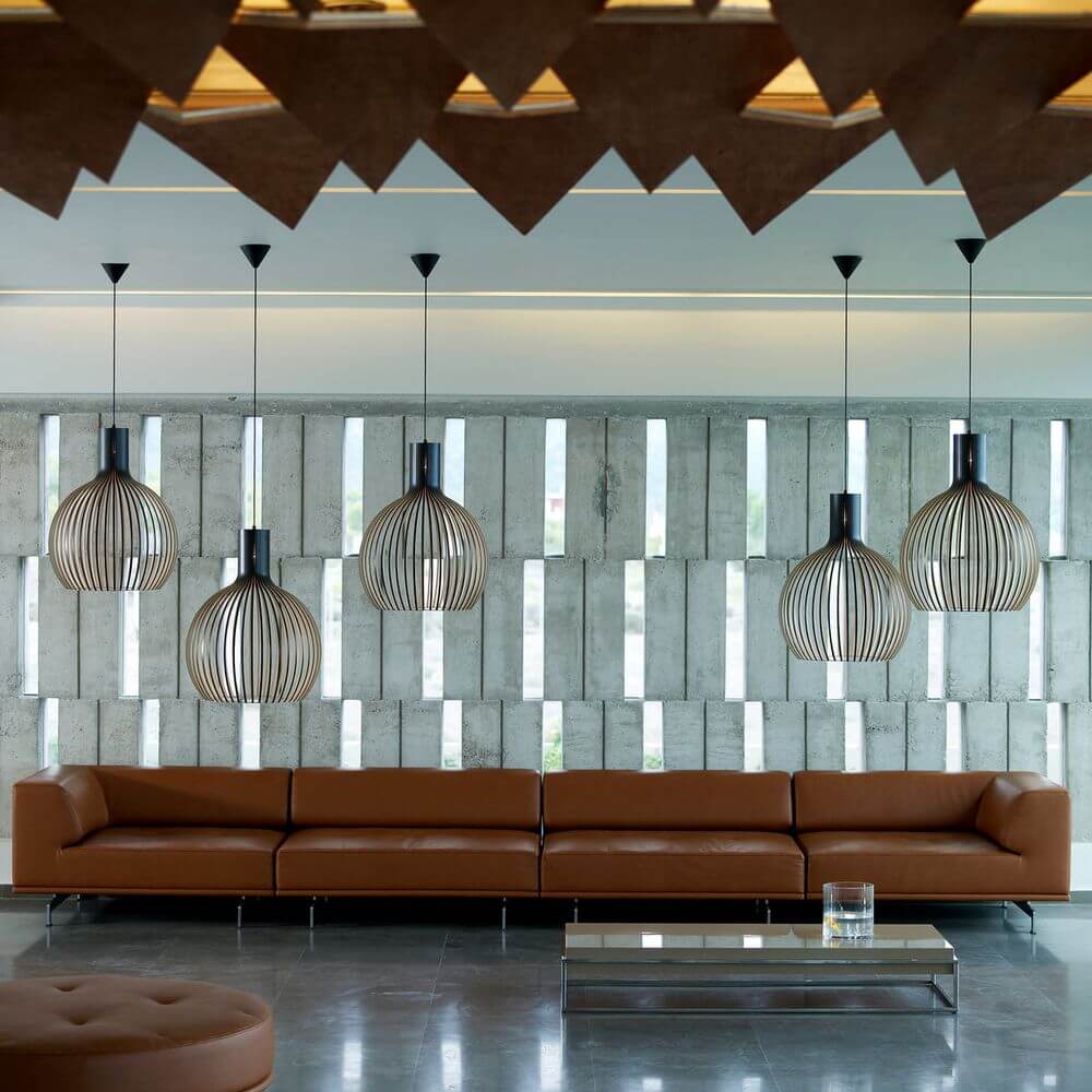 Moderne Holzpendelleuchten in einem eleganten Wohnzimmer mit braunem Sofa und stylischer Glasplatte.