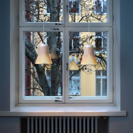 Pendant light Petite 4600 made of wood Ø 20cm above a window with a view of trees and buildings, stylish interior lighting.