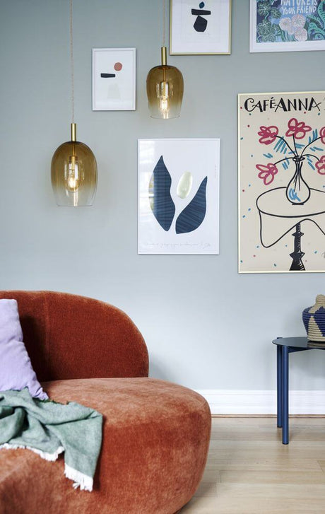 Uma 23 pendel og sofa i en moderne stue med farverige billeder på væggen.