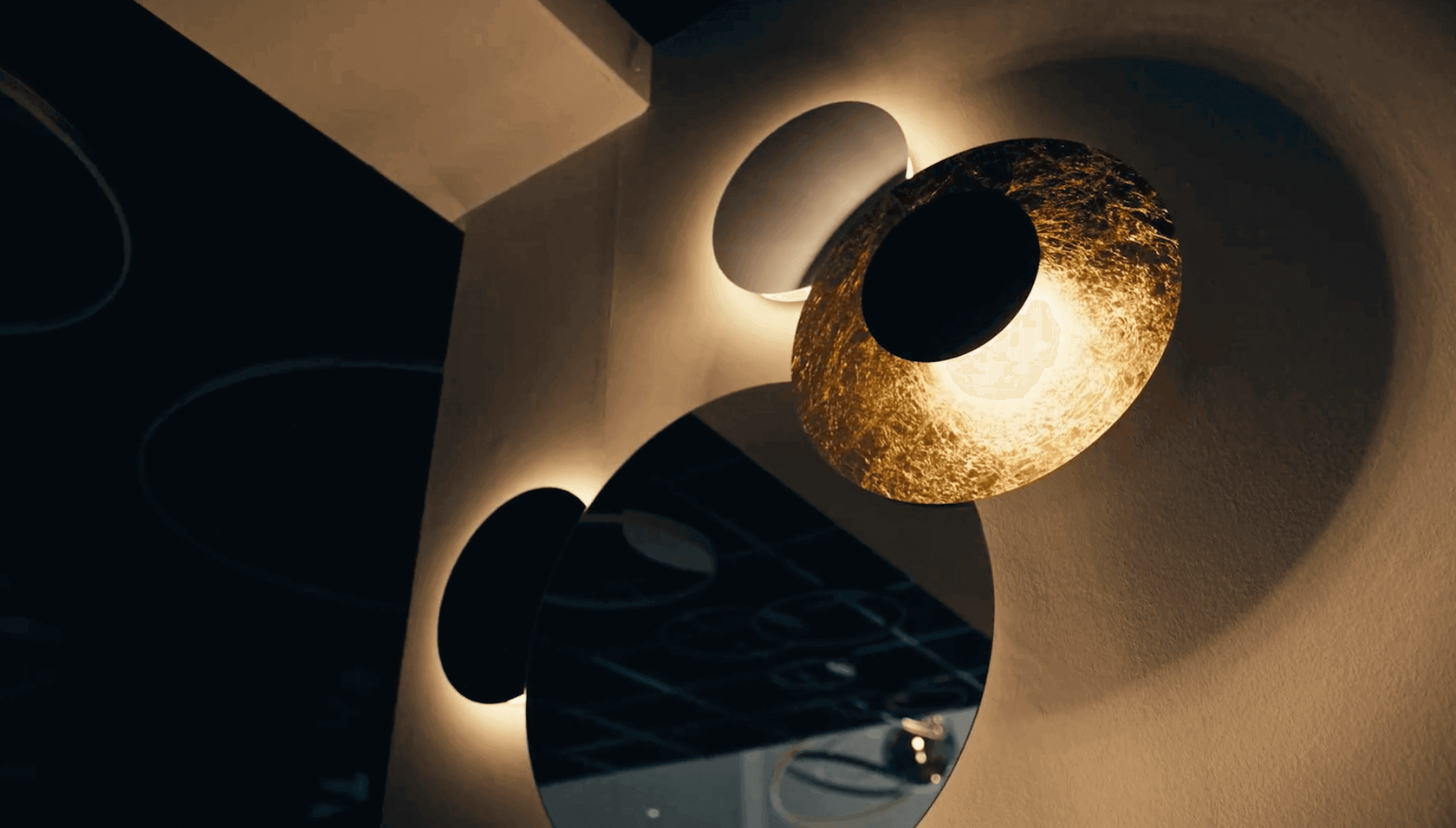 Moderne Wandbeleuchtung in goldenen und schwarzen Farbtönen, stilvoll reflektiert in runden Spiegeln.