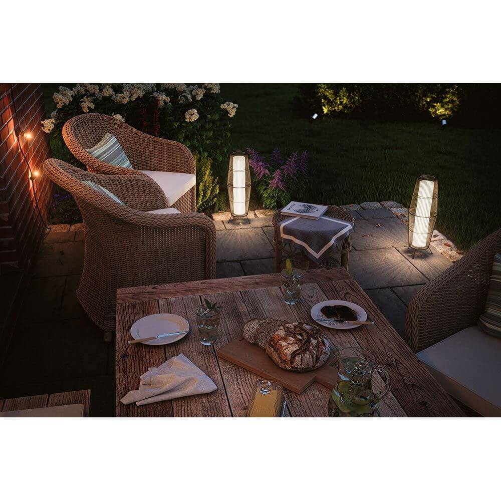 Gemütliche Gartenlandschaft mit Plug & Shine LED Lichtobjekten und Rattanmöbeln bei Nacht.