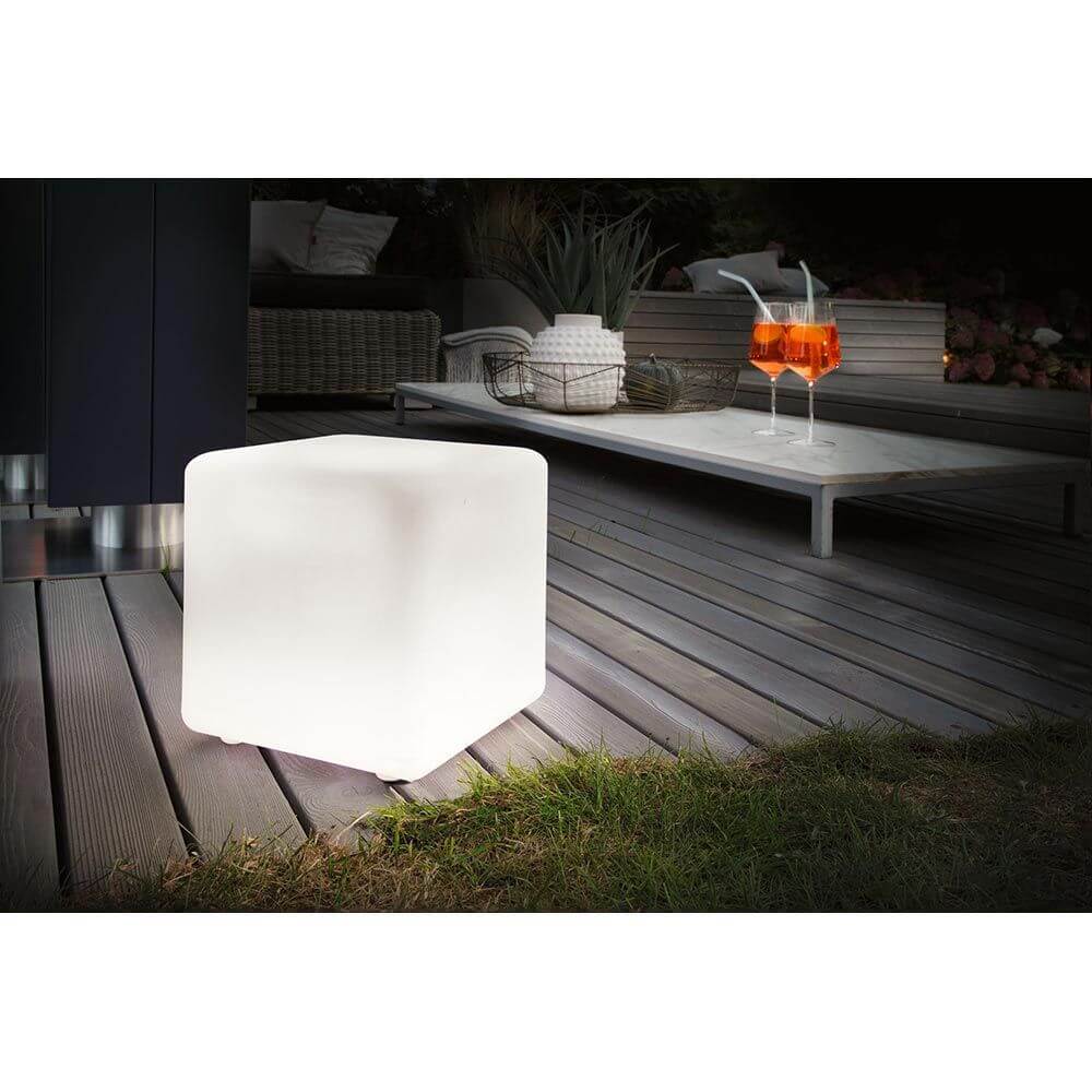 Beleuchteter Plug & Shine LED Cube in Weiß auf Holzdeck vor Terrasse mit Cocktails.