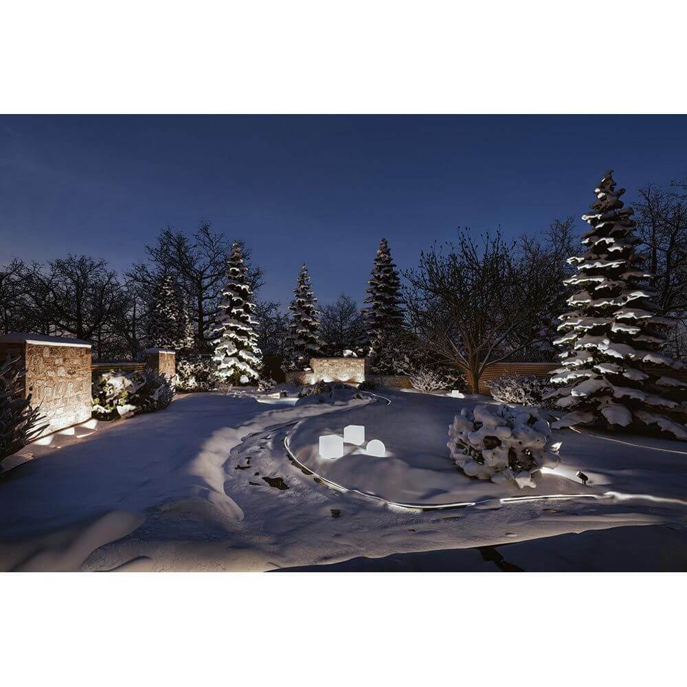 Beleuchteter Garten im Winter mit schneebedeckten Bäumen und Plug & Shine Lichtobjekten unter einem klaren Nachthimmel.
