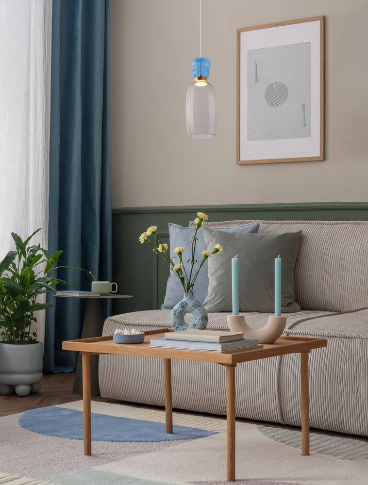 Pluma LED Pendelleuchte Ø 15cm 3000K Mehrfarbig über einem modernen Wohnzimmer mit Sofa und Tisch.