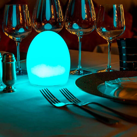 Candeeiro de mesa Point Aida Akku LED com controlo por aplicação em iluminação azul sobre uma mesa com copos.