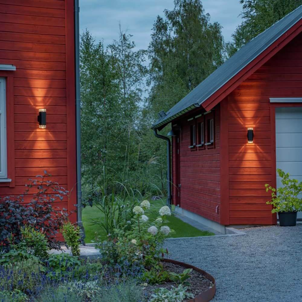 Pollux Wandleuchte 2-flammig an rotem Holzhaus im Garten beleuchtet den Eingangsbereich.