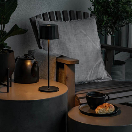 Positano Outdoor LED Akku Tischleuchte auf einem modernen Tisch neben einer Tasse und einem Croissant im Freien.