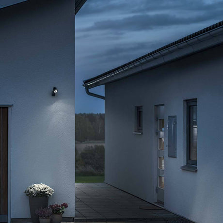 Lampa ścienna LED Prato na baterie z czujnikiem czarna IP44 zamontowana na ścianie domu o zmierzchu.
