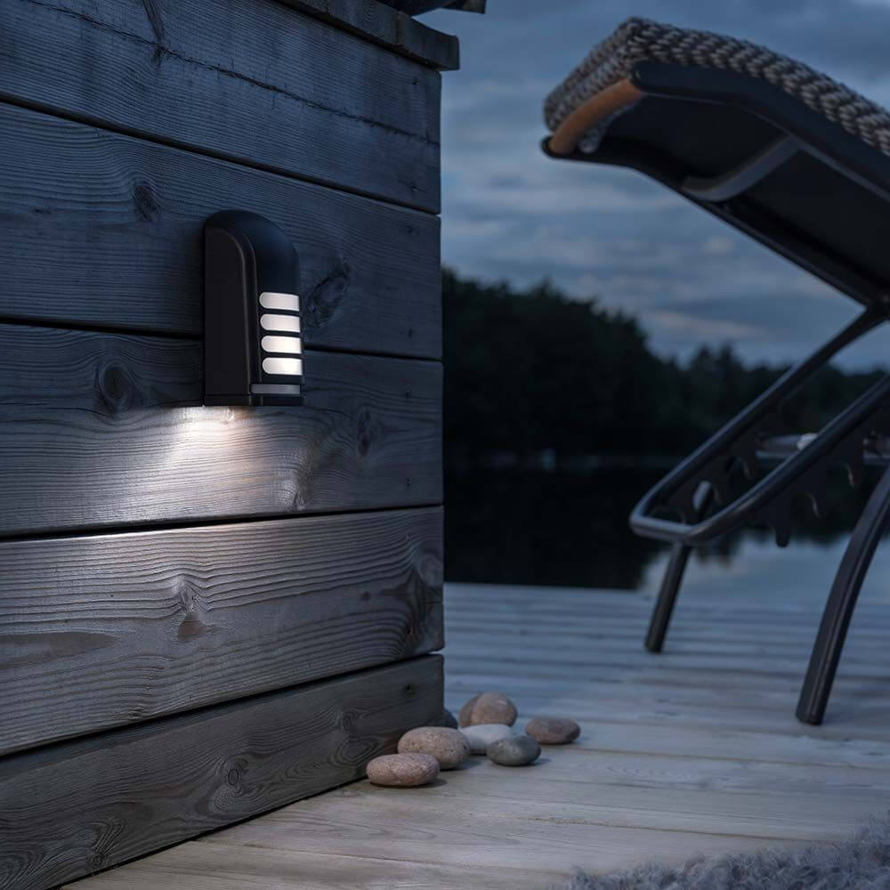 Prato Batterie LED Sensor Außen-Wandaufbauleuchte Schwarz an einer Holzwand im Außenbereich mit schöner Beleuchtung.