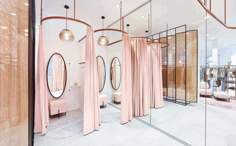 Helle Umkleidekabine mit rosa Vorhängen und runden Spiegeln in einem modernen Geschäft.