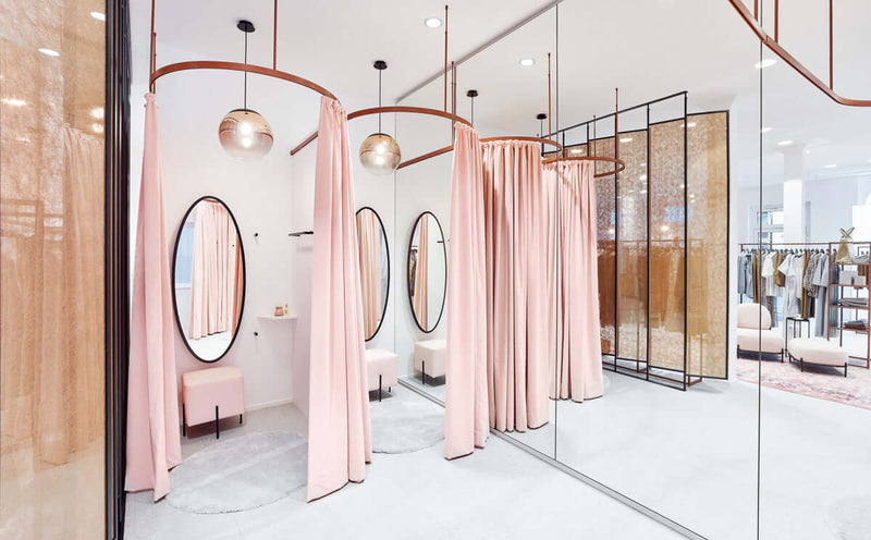 Helle Umkleidekabine mit rosa Vorhängen und runden Spiegeln in einem modernen Geschäft.