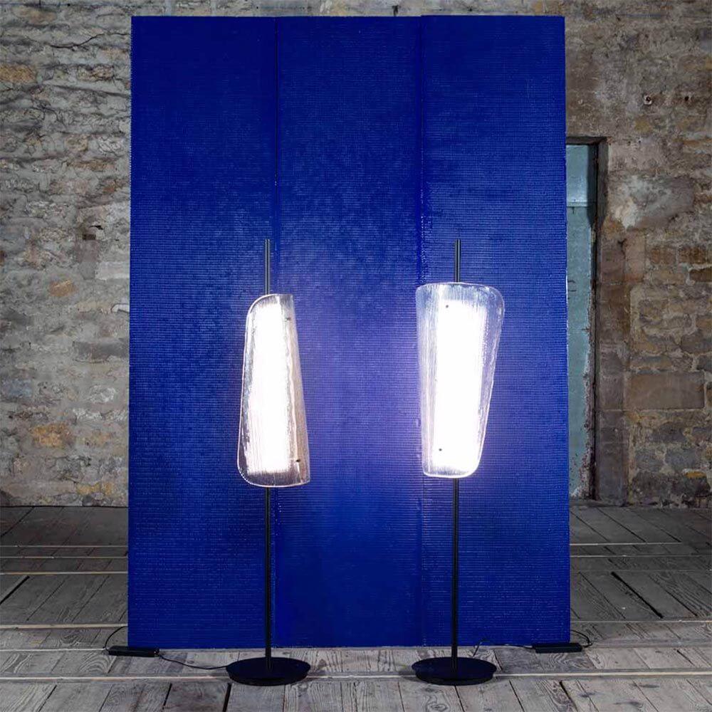 Zwei gebogene Pulpo LED Stehleuchten Bent One aus Glas vor blauer Wand im Raum.