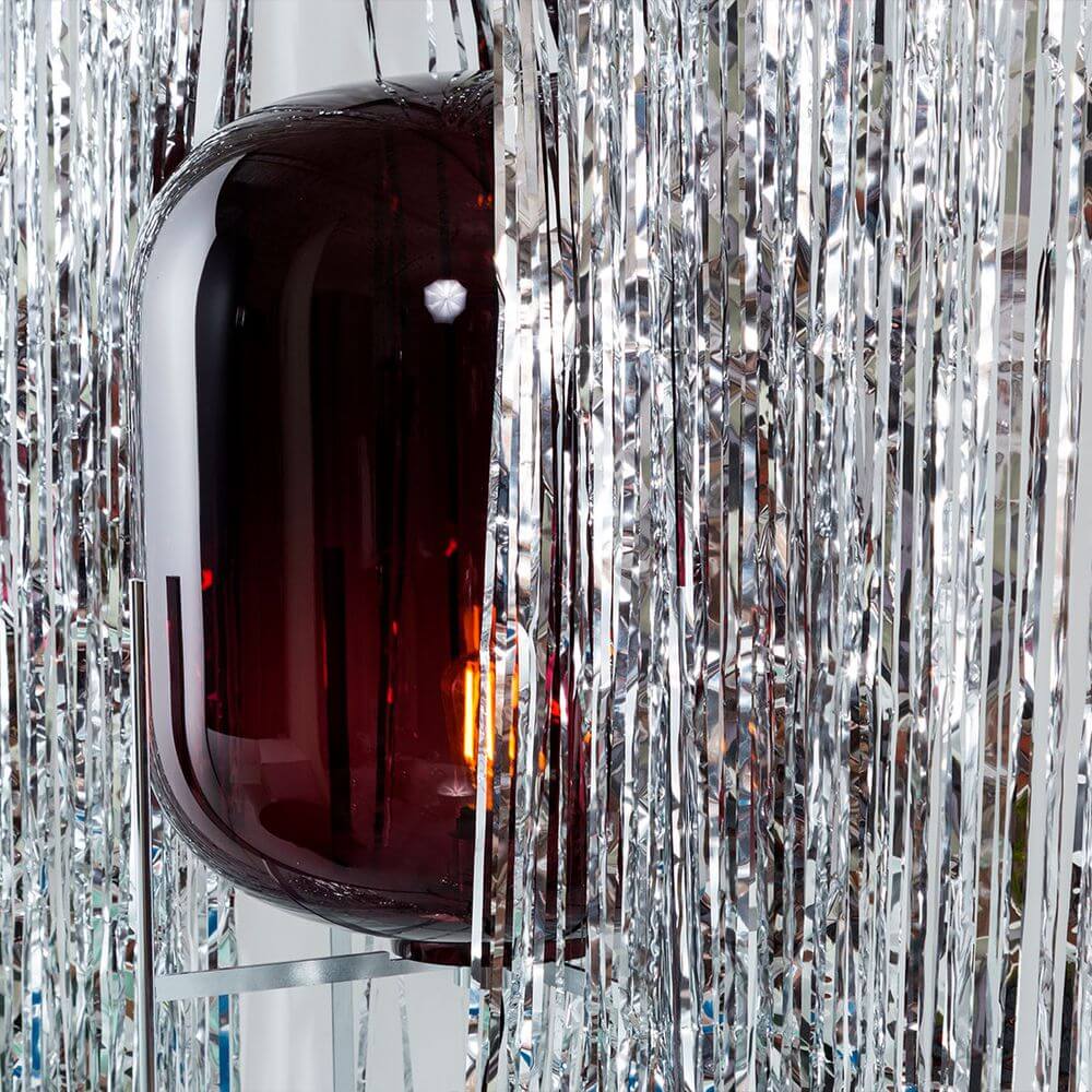 Pulpo LED Stehleuchte Oda Big mit rot-violettem Glas und silbernem Dekor umgeben von glänzenden Fransen.