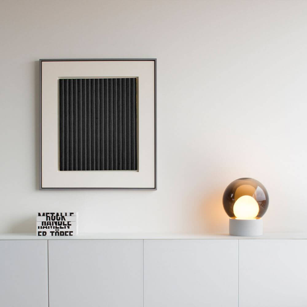 Stilvolle Boule Tischlampe von Pulpo auf einer Kommode neben quadratischem Kunstwerk und dekorativem Buch.