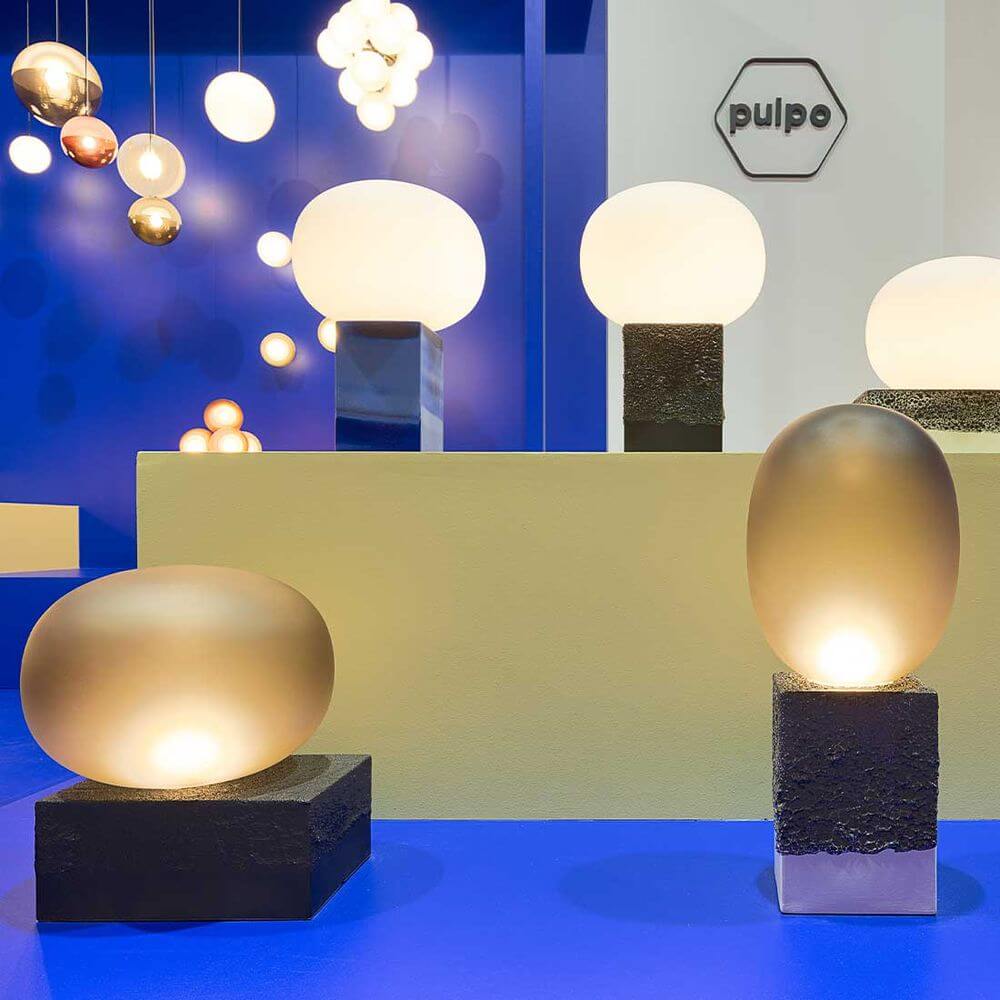 Pulpo LED Tischlampe Magma One auf einem blauen Hintergrund, Designs mit glattem und rauem Glas.