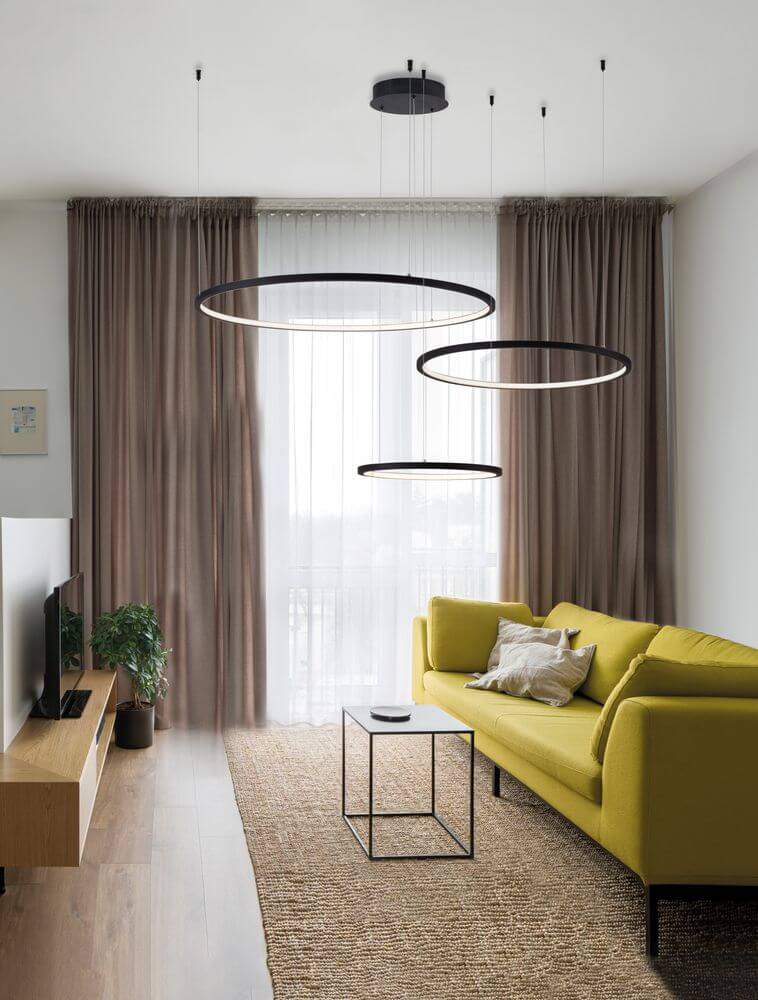 Purple LED Pendelleuchte 3-flammig Ø 130cm 3000K über einem modernen gelben Sofa im Wohnzimmer.
