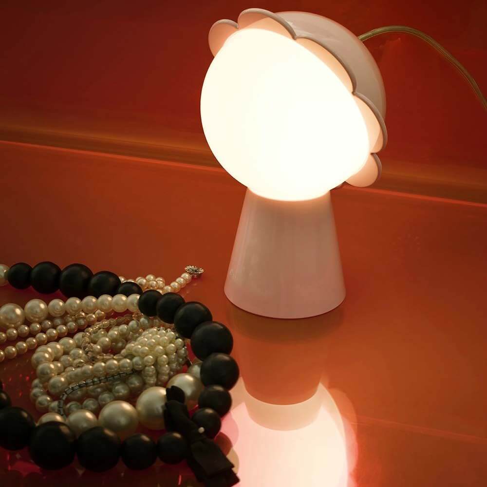 Daisy Tischleuchte mit sanftem Licht auf einem Tisch neben Perlenketten.