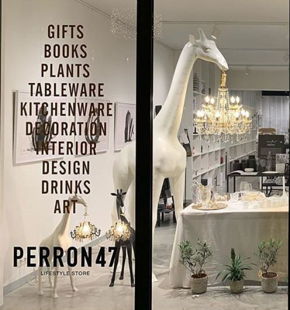 Giraffe in Love M Stehleuchte 265cm in einem stilvollen Einrichtungsladen, mit Kronleuchter im Maul.