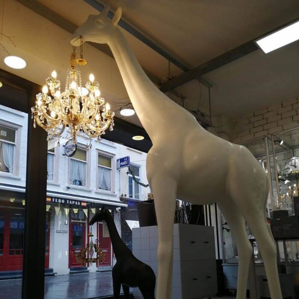 Giraffe in Love M Stehleuchte 265cm mit Kronleuchter im Maul, stilvolles Design in einem modernen Raum.