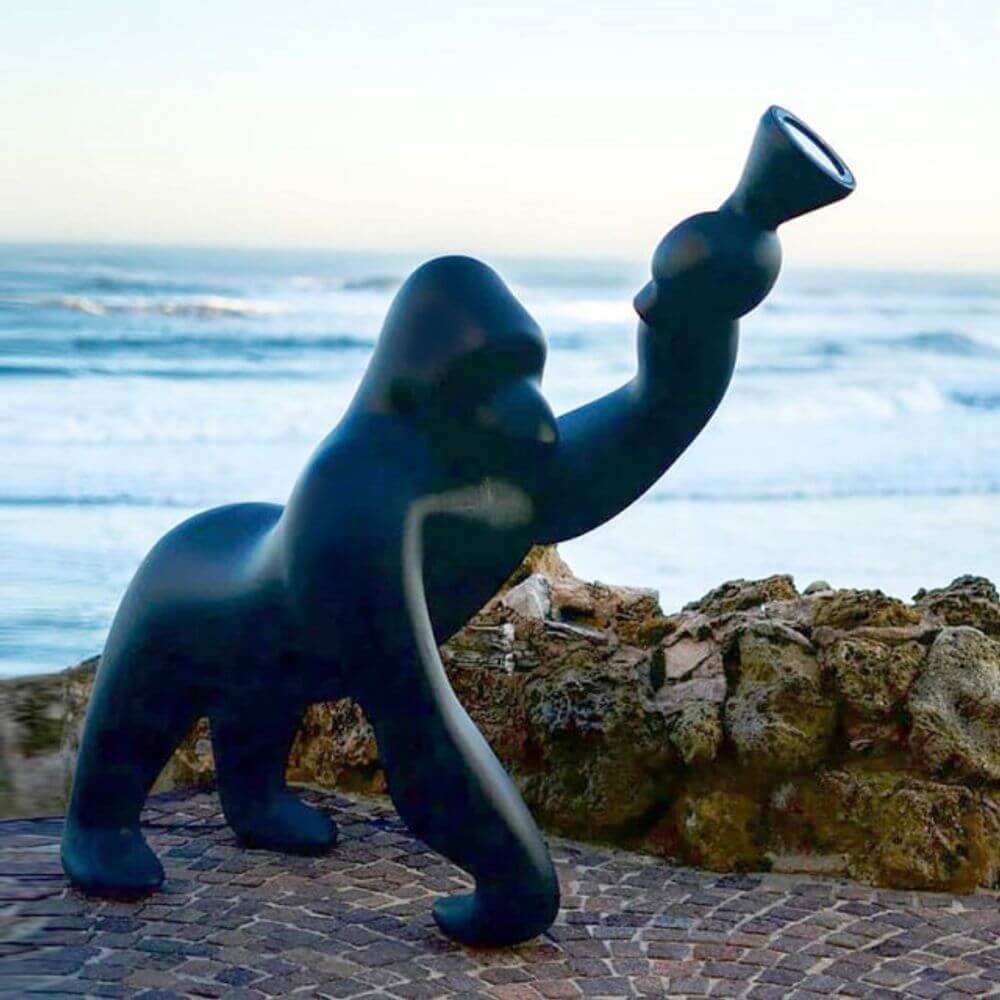Kong XL Bodenleuchte Gorilla in schwarz am Strand mit Meer im Hintergrund und erhobenem Leuchtenarm.