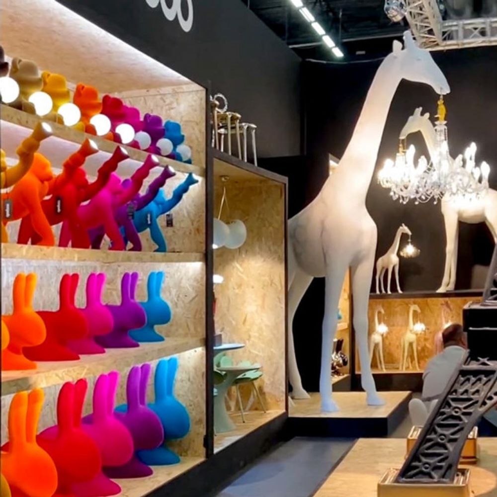 Farbenfrohe Tischlampen und Kreaturen, darunter eine große Giraffe, in einem modernen Ausstellungsraum.