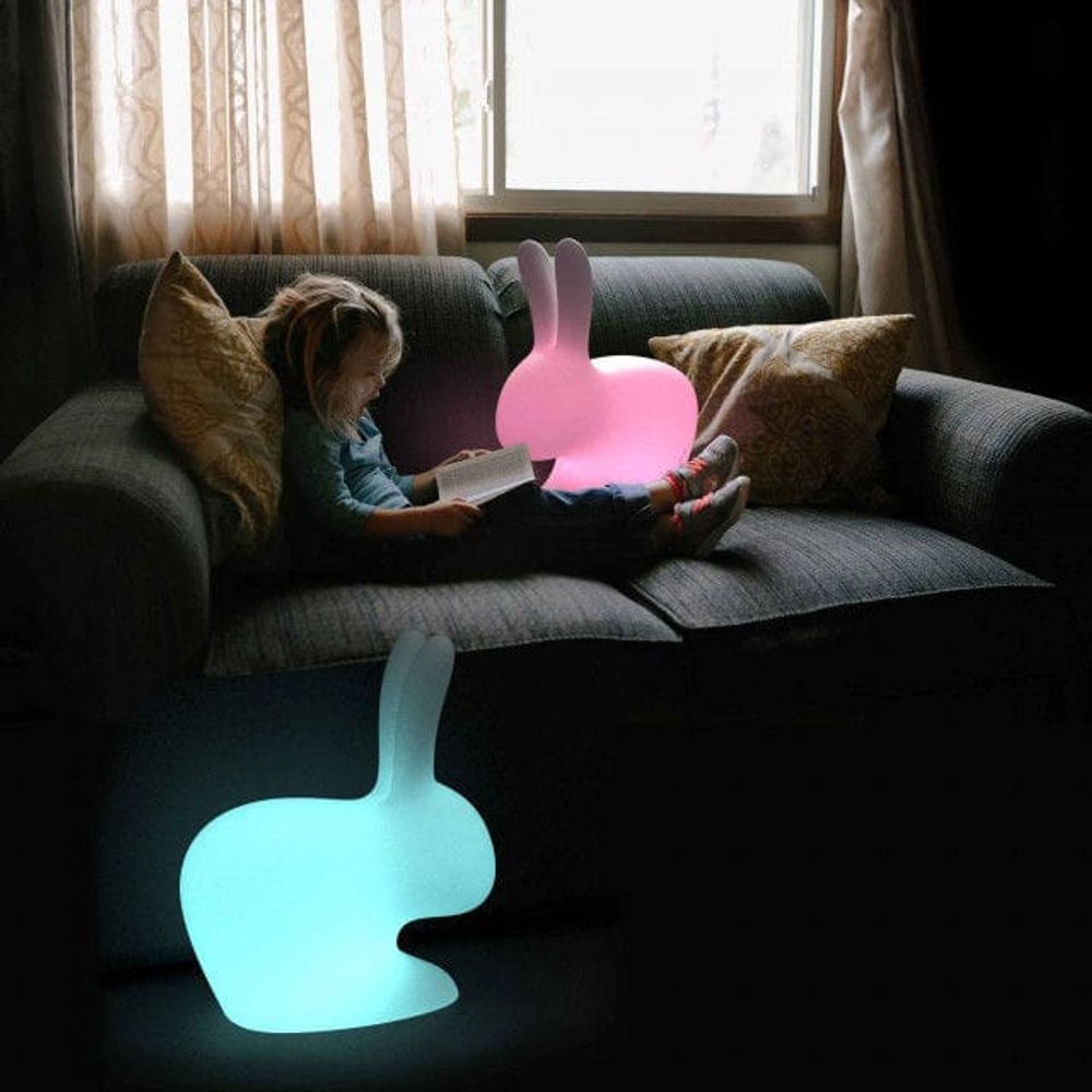 Ein Kind sitzt auf einem Sofa mit der Rabbit LED Dekolampe, die in bunten Farben leuchtet.