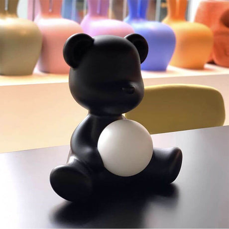 Teddy Girl rechargeable table lamp in the shape of a teddy bear with a glowing sphere on a table.