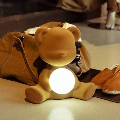 Teddy Girl Velvet Akku Tischleuchte auf Tisch mit leuchtender Kugel und Tasche im Hintergrund.