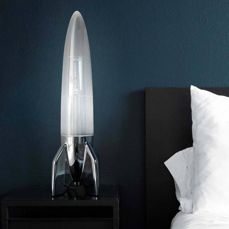 V-2 Schneider rocket table lamp on a bedside table in front of a blue wall, modern design with nostalgic flair.