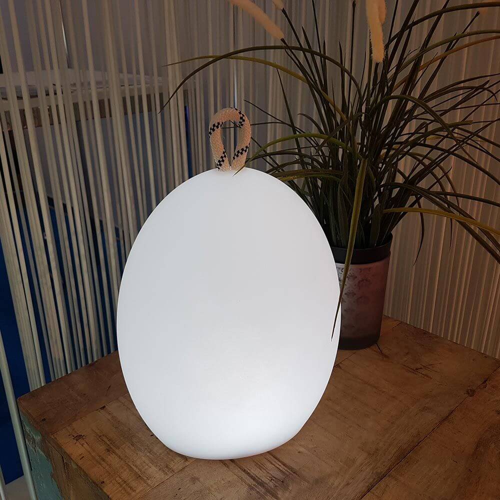 RGB-LED utendørs batterilampe Amande Corde 28 cm med app-styring på et trebrett, omgitt av planter.